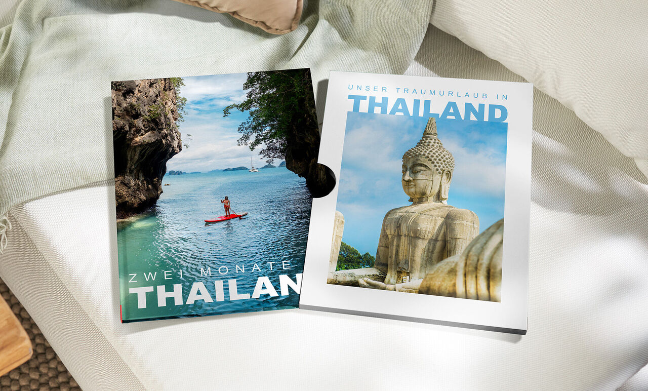 Ein CEWE FOTOBUCH Thailand mit Kajakfahrerin und Buddha-Statue auf den Covern neben passendem Schuber
