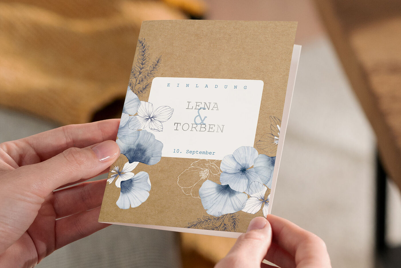 Händedemonstration einer CEWE Grußkarte zur Hochzeit mit floralen Details und Namen.