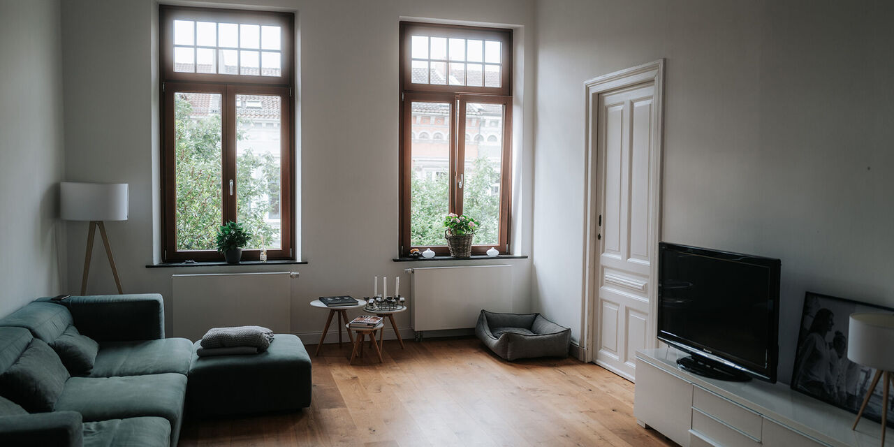 Heller Wohnraum mit grüner Couch, Fenstern und Fernseher.