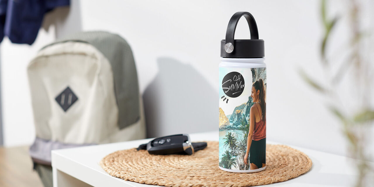 Eine stylische Trinkflasche mit einem bunten Design und einer Person davor, die in die Ferne blickt. Im Hintergrund eine Tasche und ein Tisch.