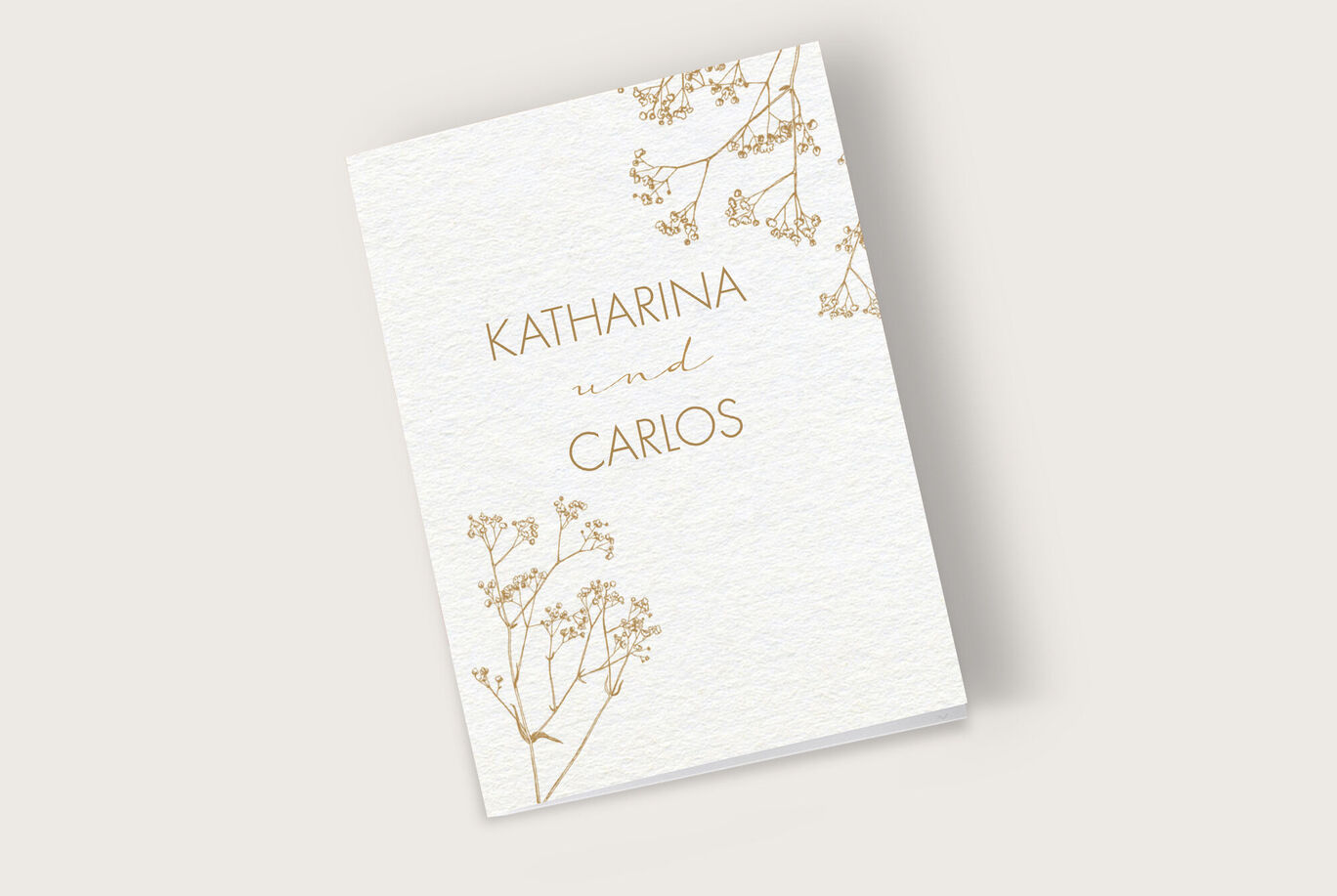 Elegante Einladungskarte mit dem Namen "Katharina und Carlos" in goldener Schrift, umgeben von zarten Blumenmotiven