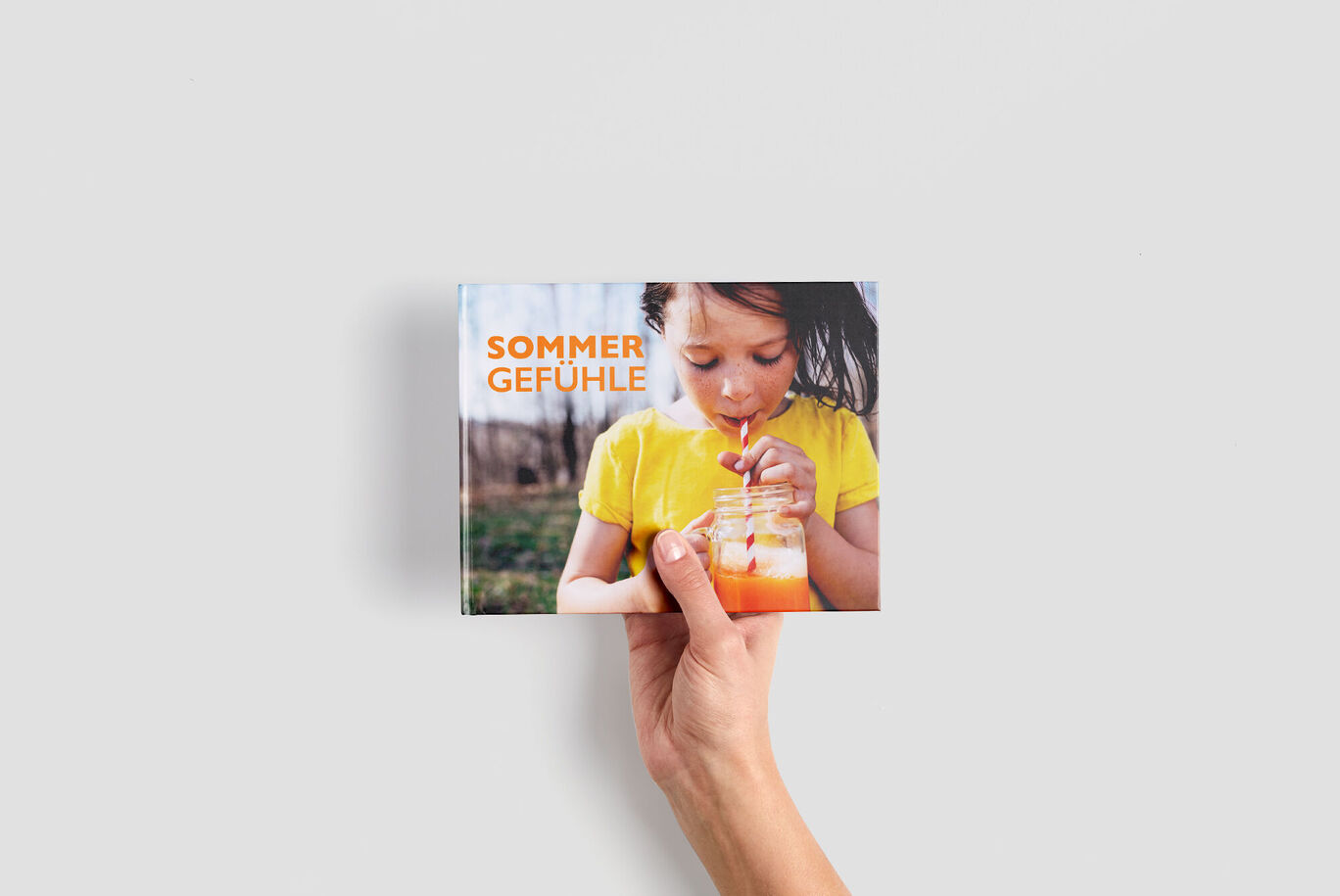 Eine Hand hält ein Fotobuch mit dem Titel 'Sommergefühle'.