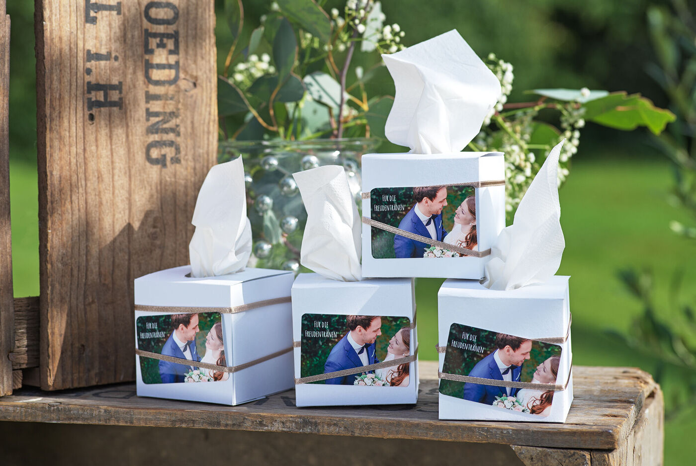 Vielfältige Geschenkboxen mit persönlichen Fotos und white Tissue-Papier auf einem Tisch im Freien, umgeben von grünen Pflanzen