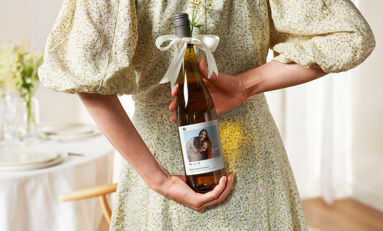 Eine Person hält eine Flasche Wein mit einer personalisierten Etikett, auf dem ein Bild und Text steht.