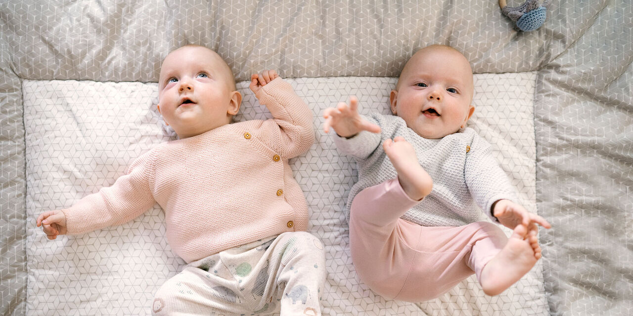 Zwei Babys liegen auf einer weichen Decke und strahlen Freude aus