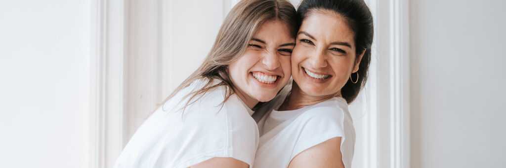 Zwei Frauen in weißen T-Shirts posieren gemeinsam und lächeln.