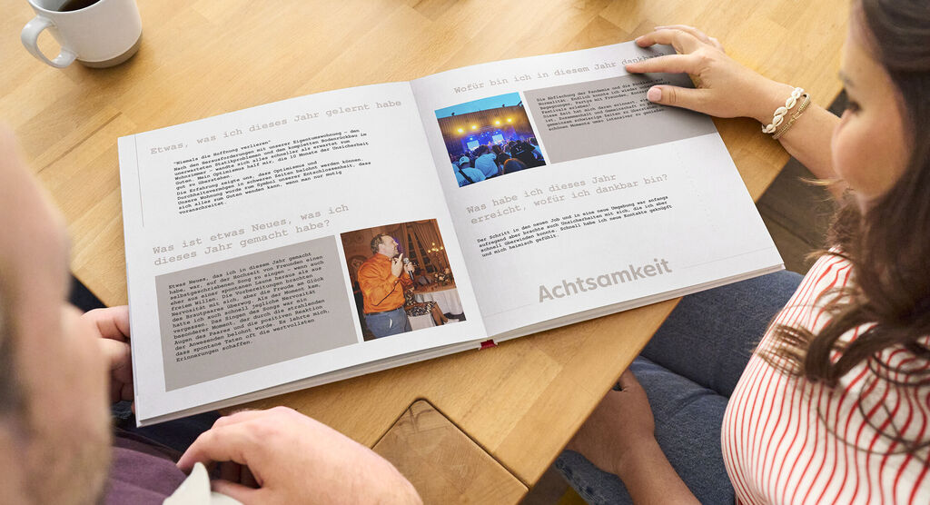 Zwei Personen blättern in einem CEWE Fotobuch auf einem Tisch.