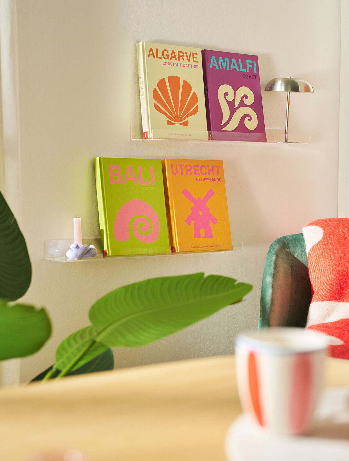 In einem Wohnzimmer hängen zwei Bilderleisten an der Wand, auf denen jeweils zwei Reisebücher in bunten Farben platziert sind.