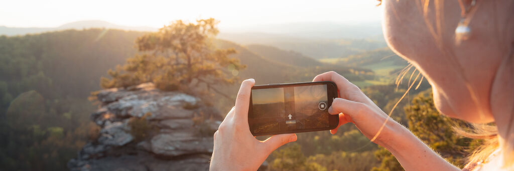 Eine Person fotografiert einen atemberaubenden Sonnenuntergang mit ihrem Smartphone auf einem Felsen in der Natur