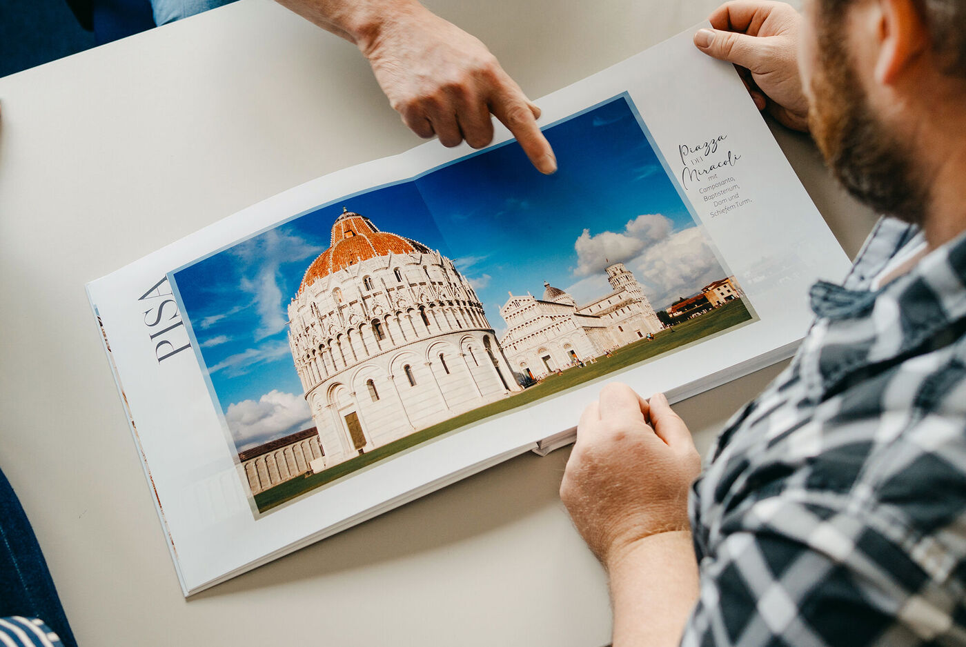 Zwei Personen betrachten ein CEWE FOTOBUCH mit einer Reisefotografie vom Schiefen Turm und der Kathedrale in Pisa