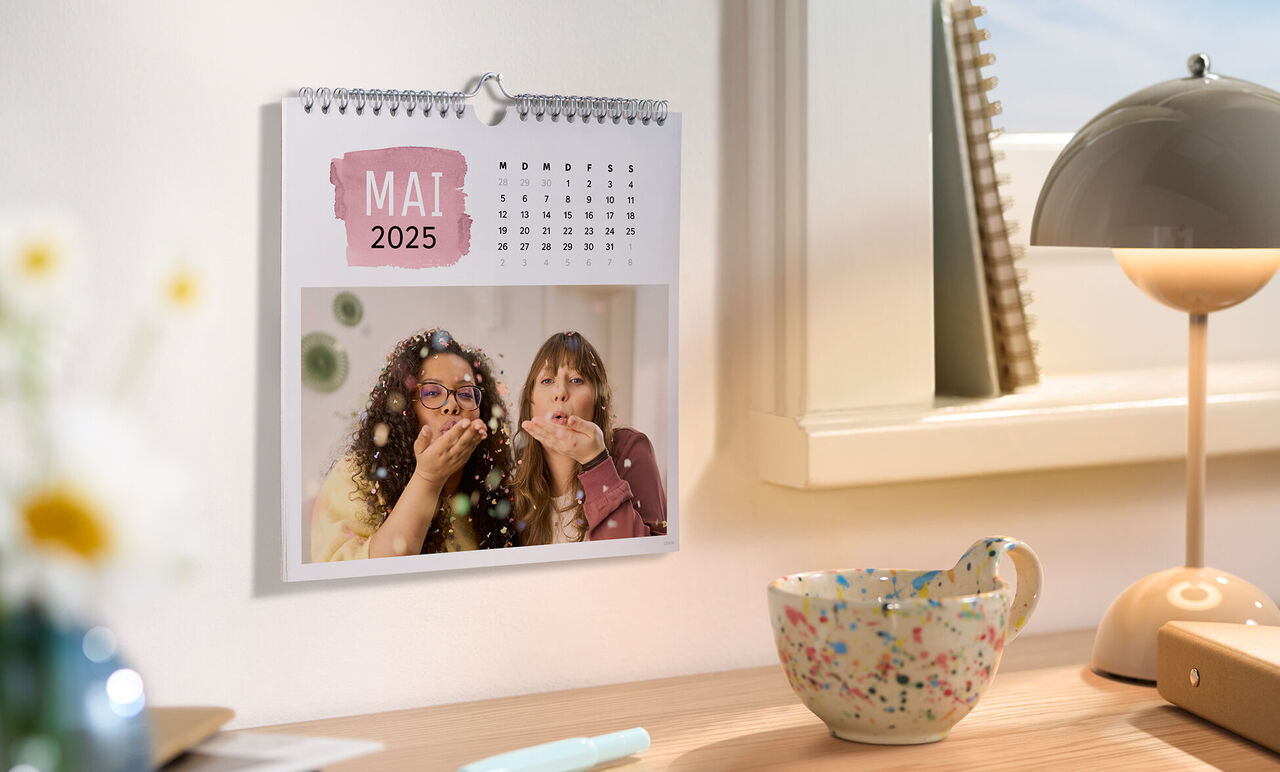 Zwei Personen in Freude mit einem CEWE Fotokalender auf dem Tisch, die den Mai 2025 zeigt