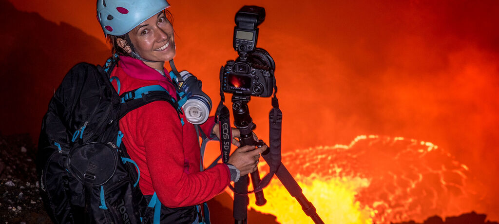 Fotograf mit Kamera und Stativ vor einem aktiven Vulkan bei Nacht