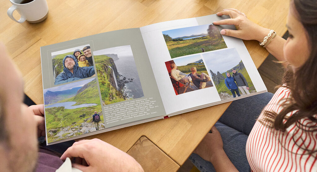 Zwei Personen schauen gemeinsam durch ein liebevoll gestaltetes CEWE Fotobuch mit Erinnerungen an Reisen und Landschaften