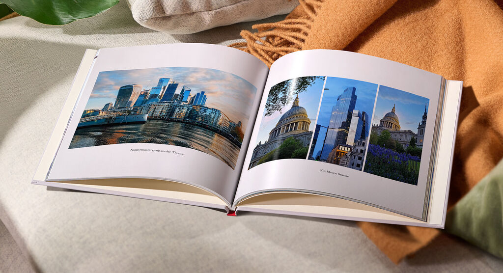 Aufgeschlagenes CEWE FOTOBUCH mit Stadtansichten und Landschaften auf der linken Seite, gemütlicher Untergrund mit Textilien.