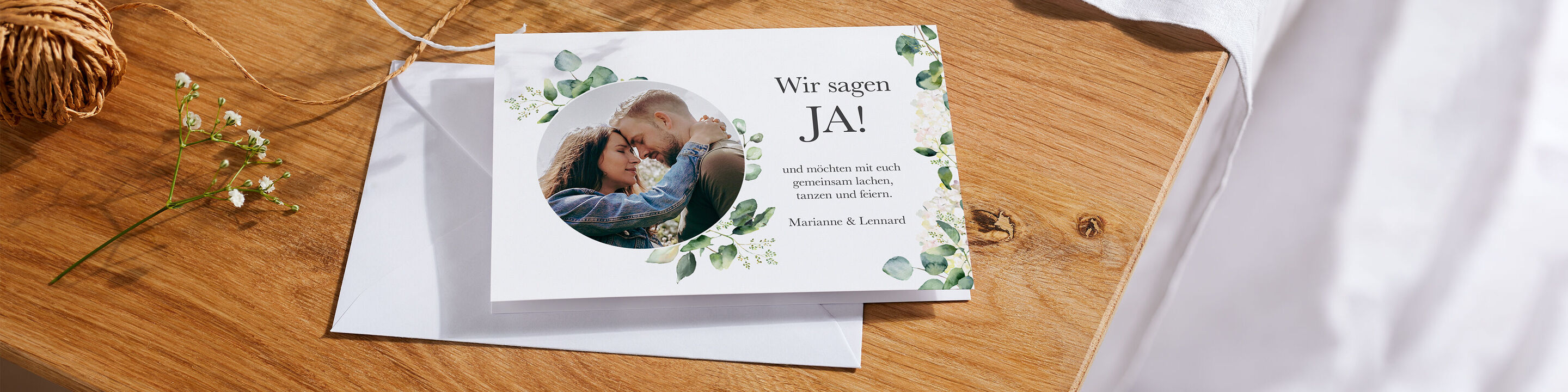 Eine romantische Einladungskarte mit einem Foto eines Paares umgeben von grünen Blättern. Sie besagt: „Wir sagen JA!“