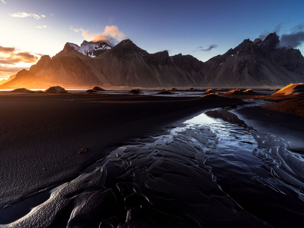 Wunderschöne Landschaft mit Bergen und Wasserlauf am Strand bei Sonnenuntergang