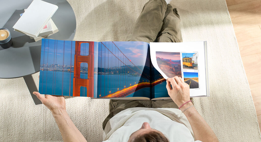 Person blättert durch ein CEWE Fotobuch mit Bildern der Golden Gate Bridge und anderer Reisemomente.