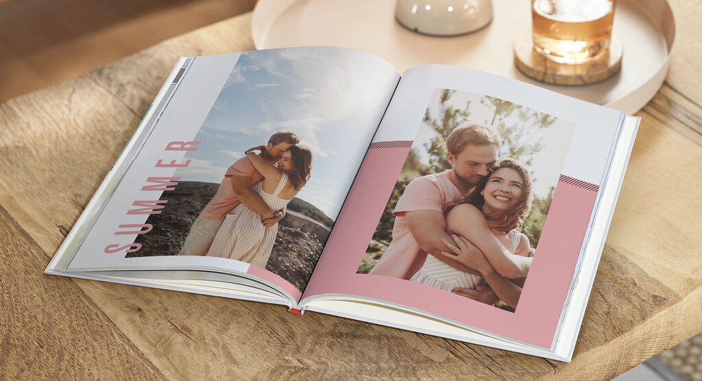 Zwei Personen umarmen sich in einem geöffneten CEWE FOTOBUCH. Es gibt eine schöne Sommerlandschaft im Hintergrund.