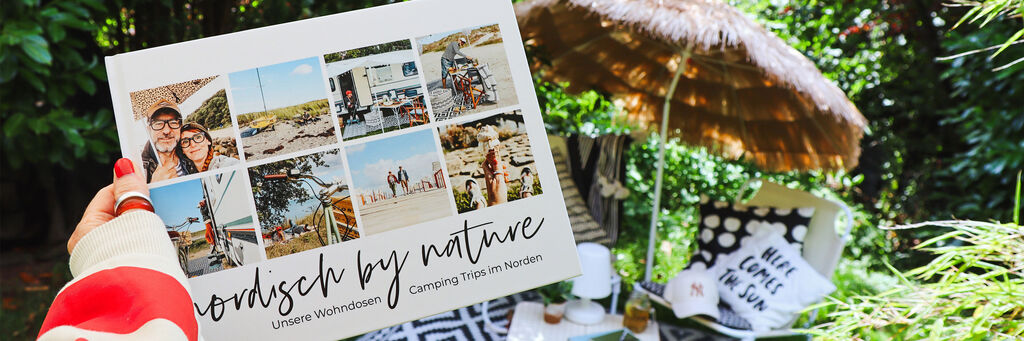 Ein Fotobuch mit Urlaubsmotiven wird in der Hand gehalten, umgeben von einem gemütlichen Outdoor-Setup.