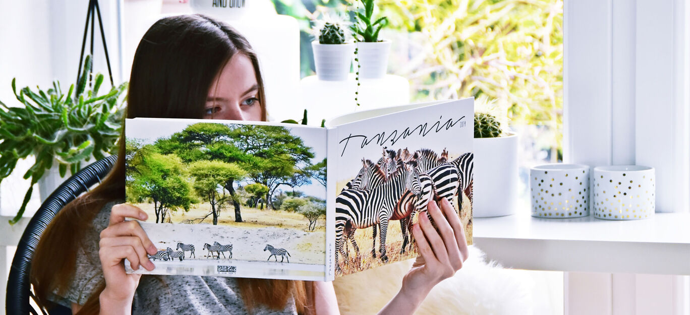 Eine Person blättert durch ein CEWE FOTOBUCH mit Tiermotiven, darunter Zebras und Landschaften.