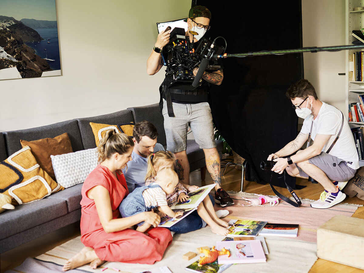 Familie liest gemeinsam in einem Fotobuch auf dem Sofa.