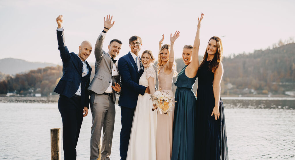 Freunde feiern mit Freude am See, in eleganter Kleidung, mit Lächeln und Winken