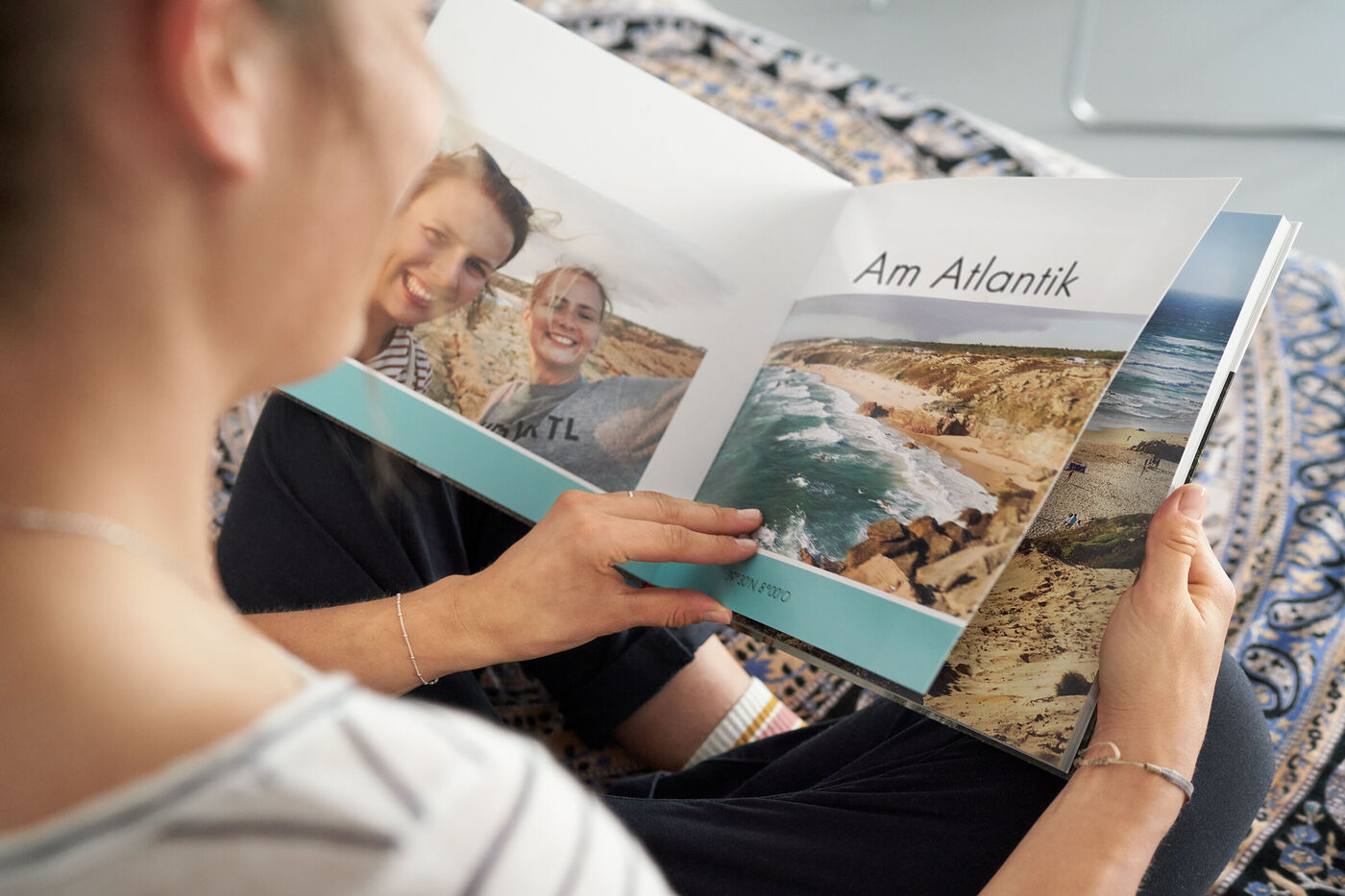 Eine Person blättert durch ein CEWE FOTOBUCH mit Bildern von einem Urlaub am Atlantik.