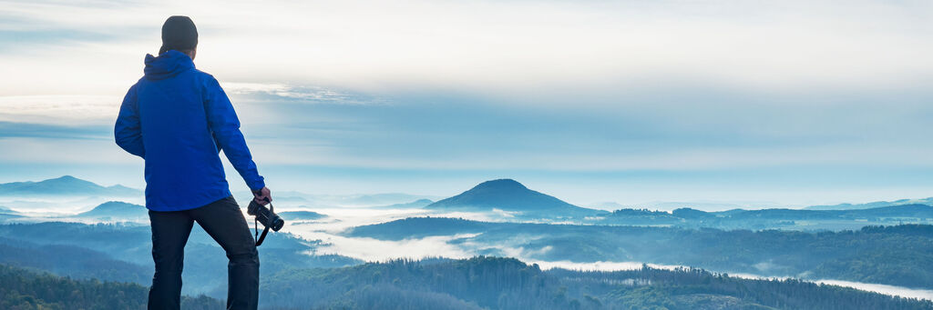 Mann mit Kamera schaut auf eine weitläufige, neblige Landschaft.