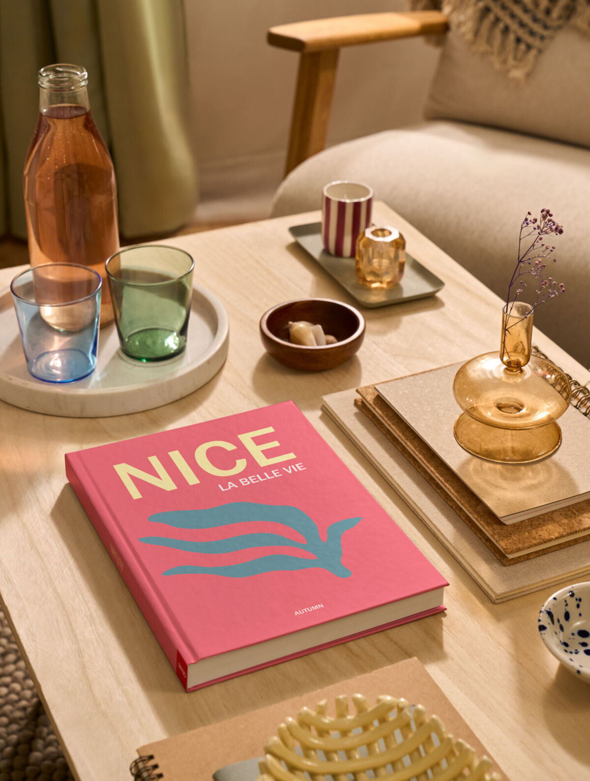 Auf einem Couchtisch liegt ein CEWE FOTOBUCH. Das Cover ist pink und mit dem Schriftzug „Nice“ gestaltet.