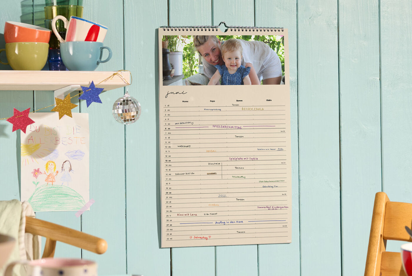 CEWE-Fotokalender als Familienplaner hängt an der Wand, Monat Juni mit Terminen und Foto oben sichtbar