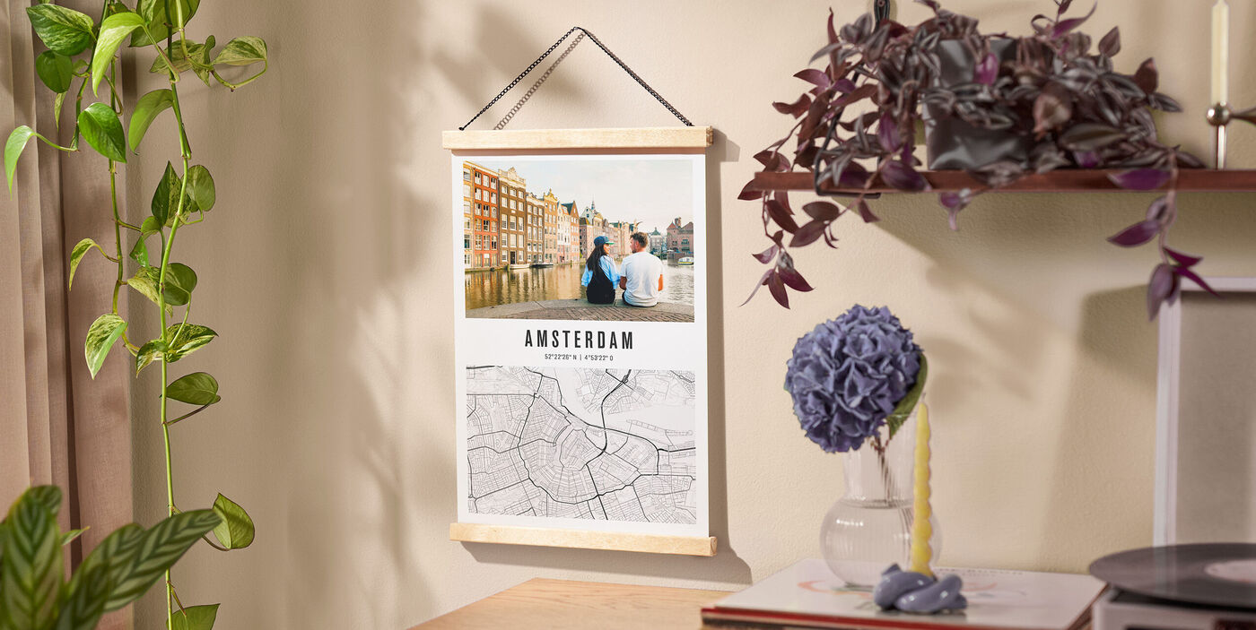CEWE Poster mit Stadtkarte von Amsterdam und Foto, an heller Wand neben Regal mit Pflanze hängend