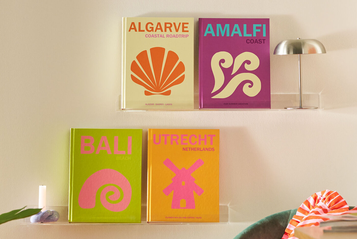 Vier farbenfrohe Reisefotobücher mit den Titeln Algarve, Amalfi, Bali und Utrecht stehen auf einem Regal