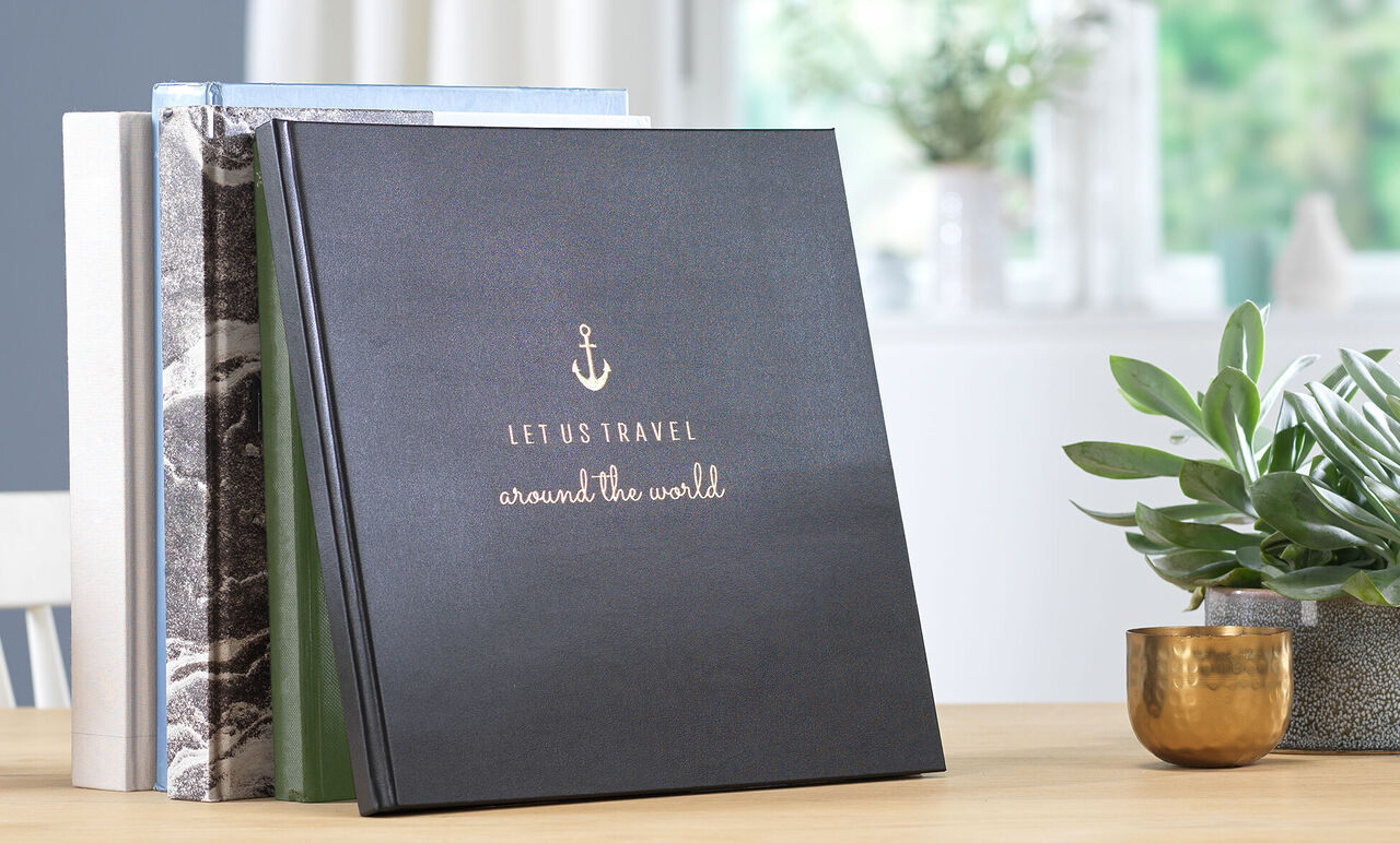 Drei stehende CEWE FOTOBÜCHER, vorderes Buch mit Anker und Reisespruch