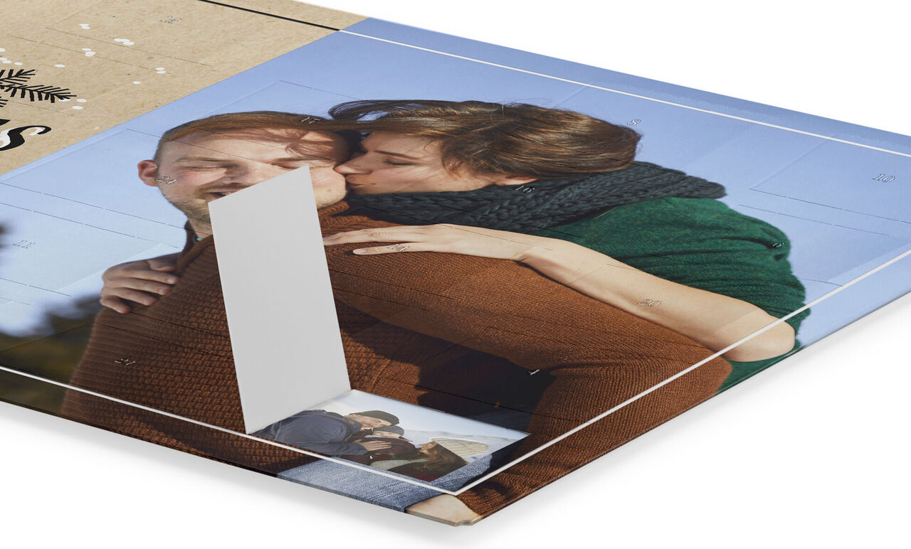 Eine Frau küsst einen Mann auf die Wange. Beide sitzen auf einem Fotobuch mit Urlaubserinnerungen.