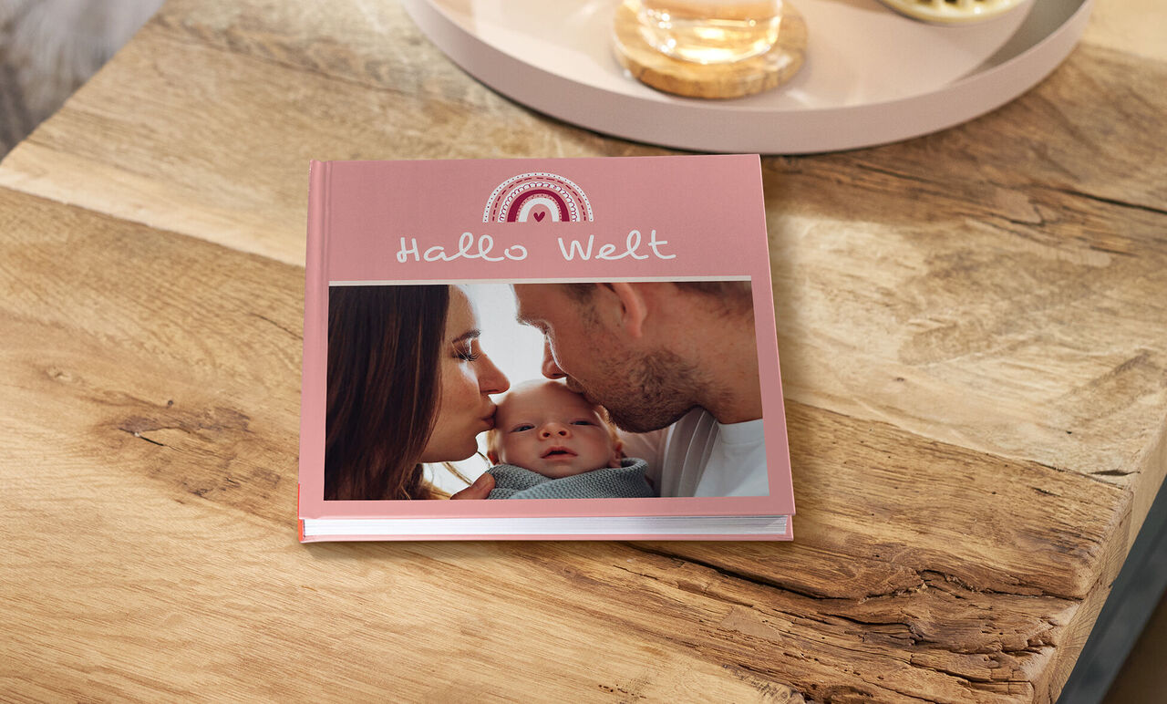 CEWE FOTOBUCH mit rosafarbenem Cover und Foto von Eltern mit Neugeborenem