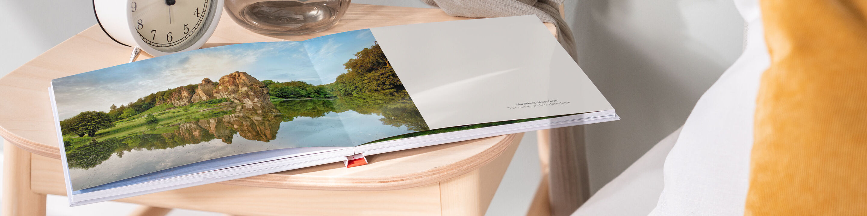 Ein geöffnetes CEWE Fotobuch zeigt wunderschöne Landschaftsfotografien auf einem Holztisch.