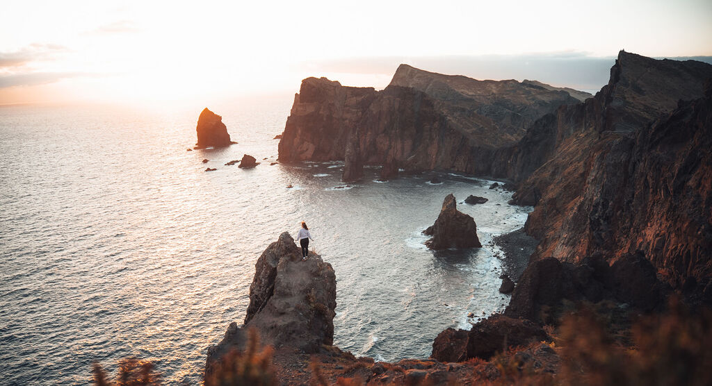 Person steht auf Felsen und blickt auf das Meer und hohe Klippen im Sonnenlicht