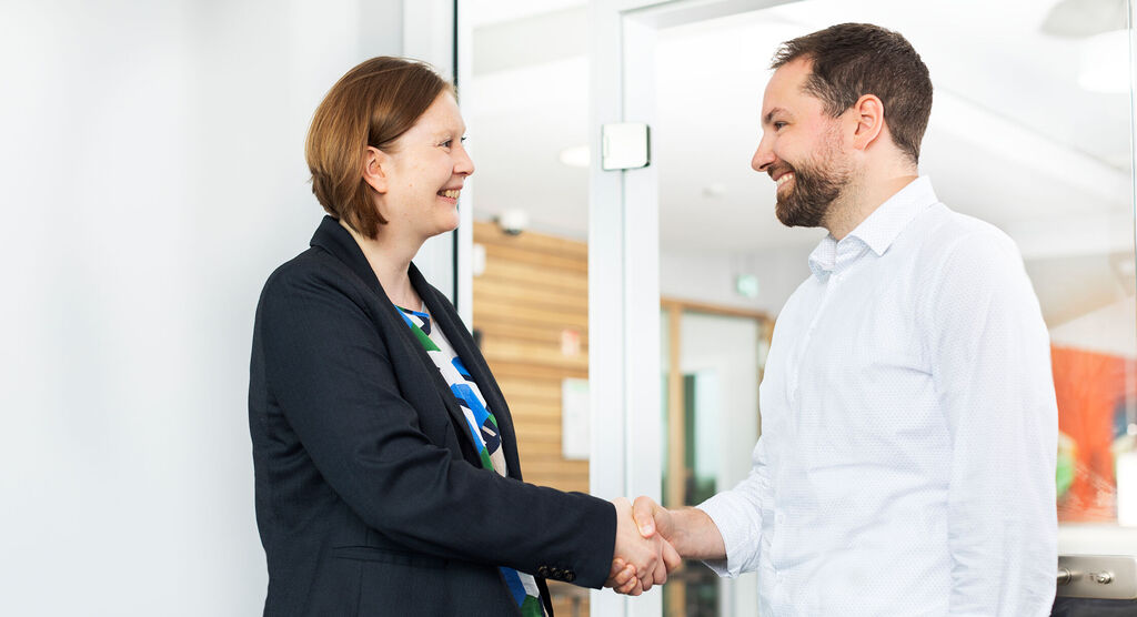 Zwei Personen schütteln sich die Hände in einem modernen Büro.