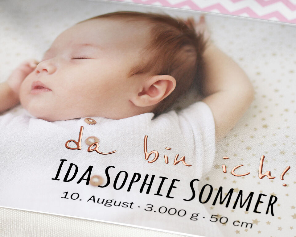 Ein süßes Baby mit einer weißen Decke im Bild, den Arm ausgestreckt.