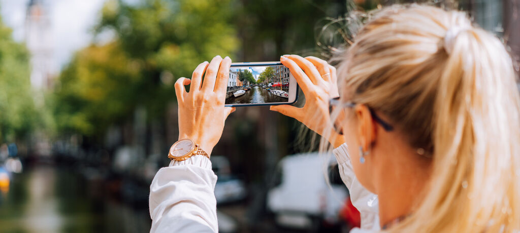 Frau fotografiert einen städtischen Kanal mit dem Smartphone.