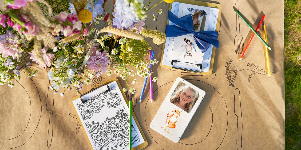 Bunte Stifte und kreative Materialien auf einem Tisch mit Fotografien und einem Blumenarrangement