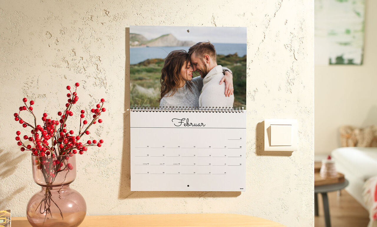 Ein liebevoller Schnappschuss von zwei Personen, die sich umarmen, vor einer malerischen Küstenlandschaft, hinter einem CEWE Fotokalender fü