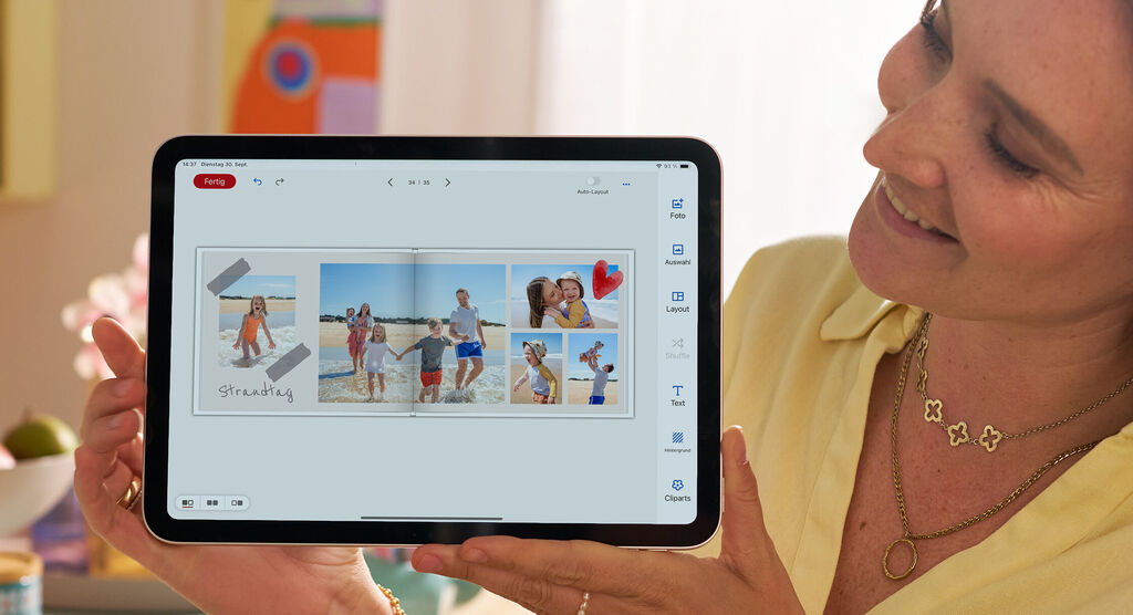 Eine Person hält ein Tablet mit einem CEWE FOTOBUCH voller Strandbilder.