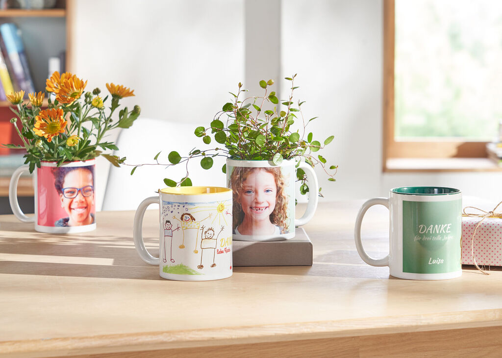 Bunte Tassen auf einem hellen Holztisch, einige mit Blumen gefüllt