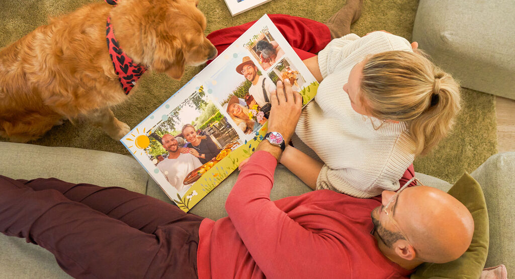 Zwei Menschen und ein Hund entdecken liebevolle Fotos und Collagen im offenen CEWE FOTOBUCH.
