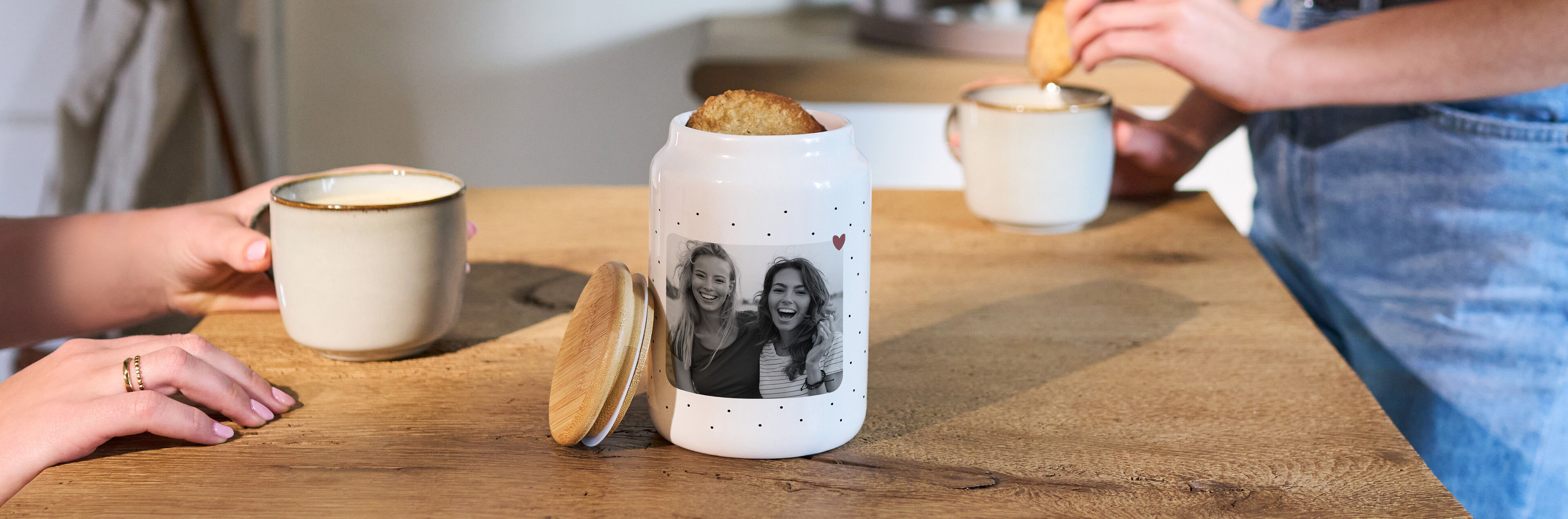 CEWE Keksdose mit persönlichem Foto steht auf einem Holztisch zwischen zwei Tassen und Gebäck