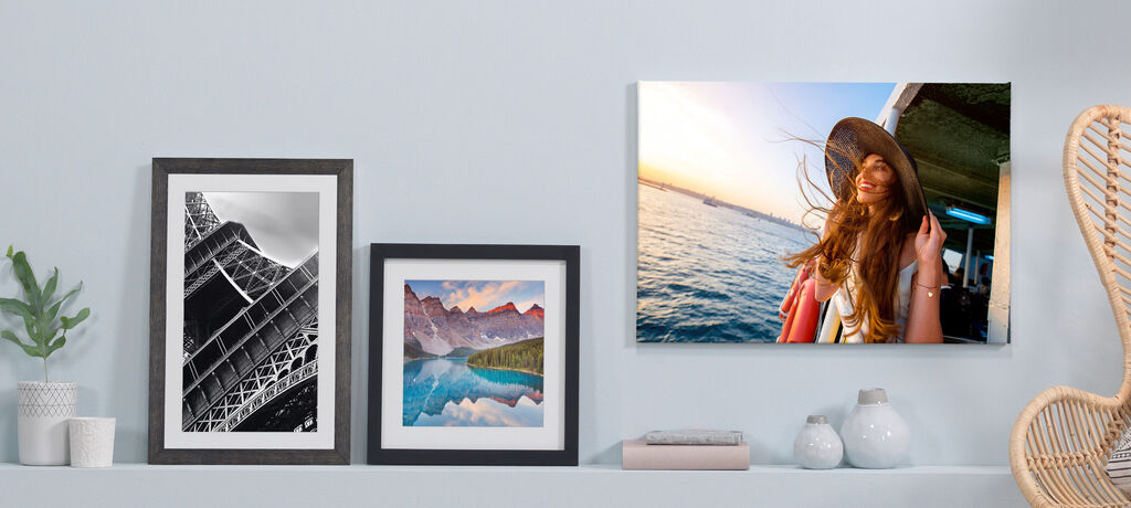 Wandbilder mit Fotos auf einem Regal, darunter eine moderne Vase und Deko-Elemente. Das rechte Bild zeigt eine Frau mit Sonnenhut am Wasser.