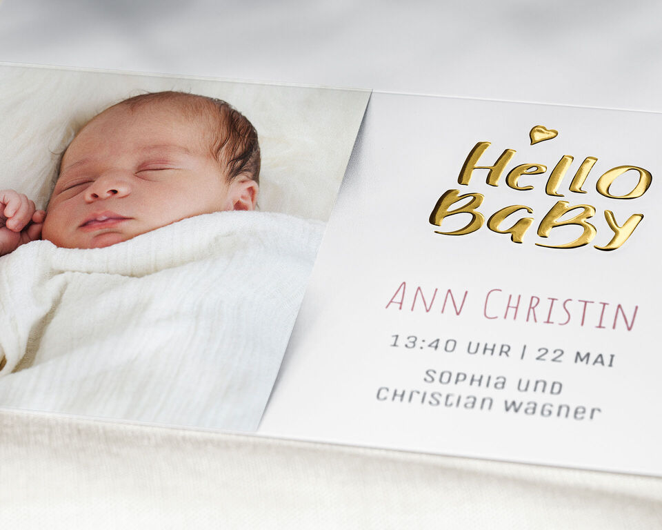 Ein hübsches Baby trägt eine weiße Decke und lächelt. Der Name "Ann Christin" ist elegant daneben geschrieben.