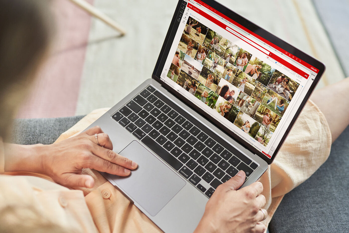 Eine Person mit blonder Haarfarbe betrachtet Bilder auf einem Laptop, umgeben von bunten Kissen. Es ist ein Moment der Freude und Kreativität.
