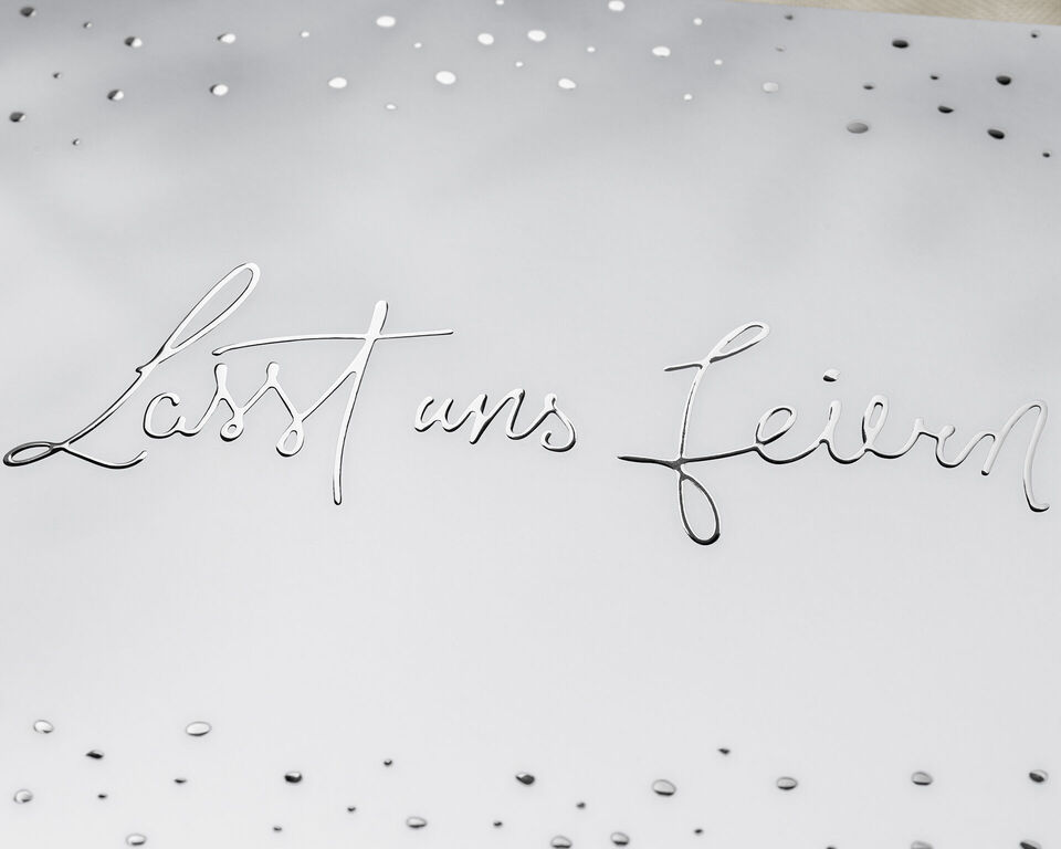 Eine silberne Schrift auf weißem Hintergrund mit der Aufschrift 'Lasst uns feiern'